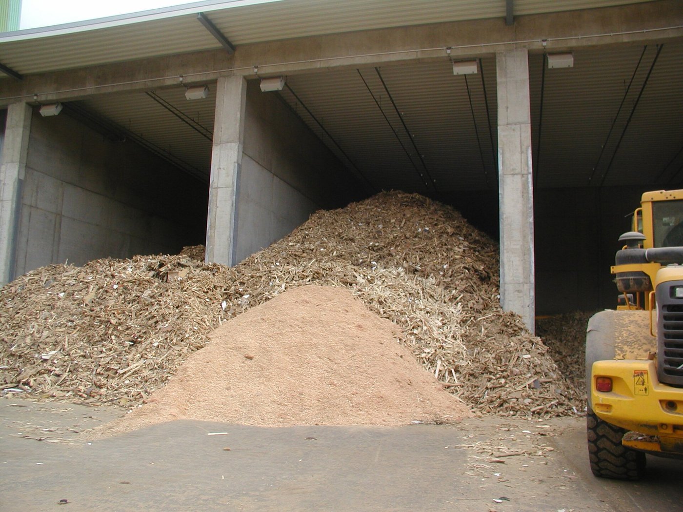 Mixed waste wood in a bunker at a recycling facility, with a loader